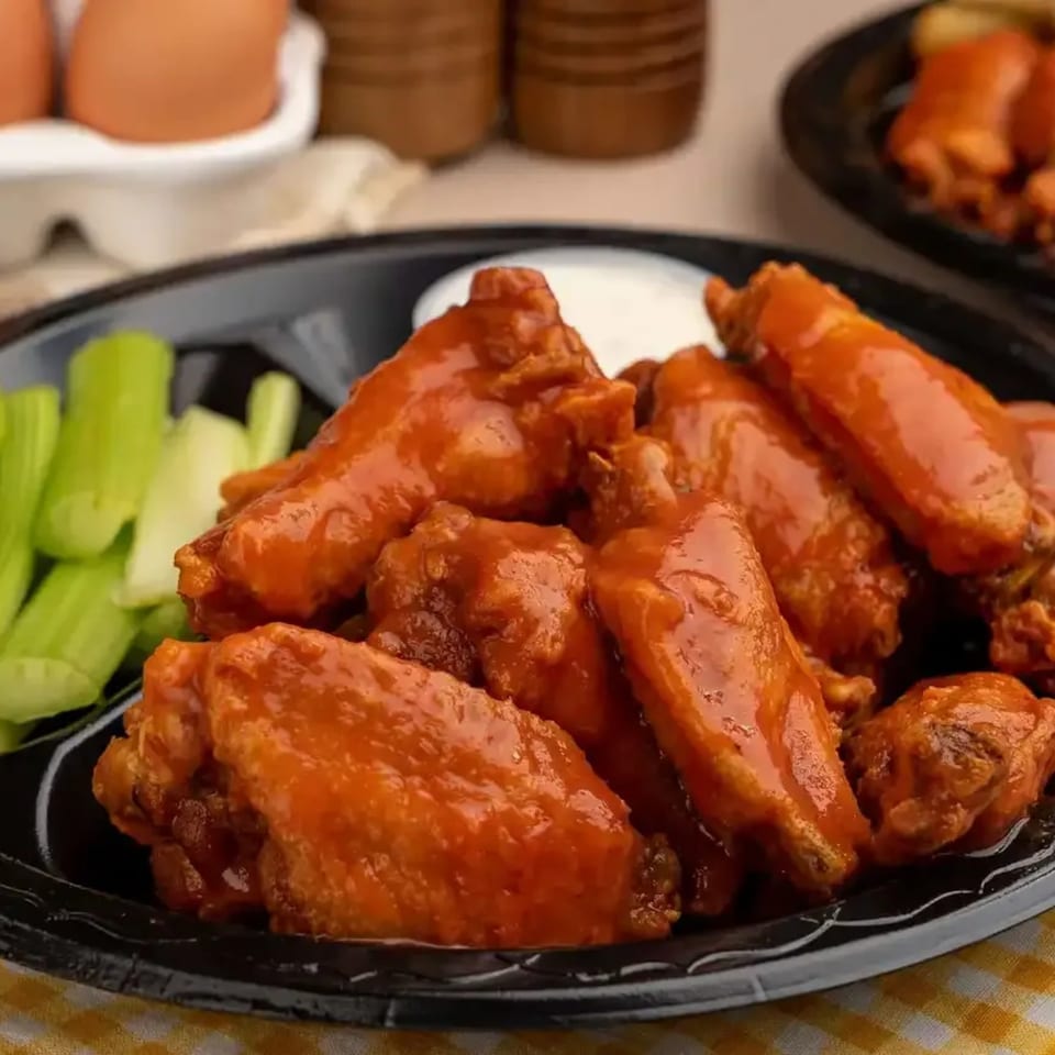 Jim Bob's Chicken Fingers' buffalo wings with celery sticks and ranch dressing on a black plate.