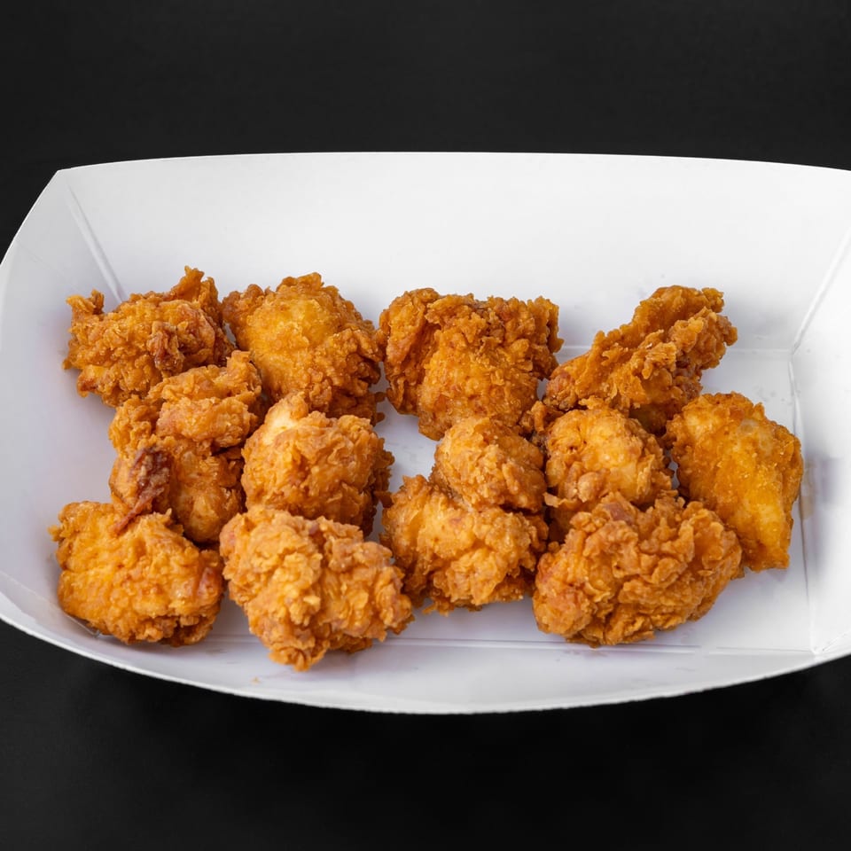 Crispy golden-brown Jim Bob's Chicken Fingers popcorn chicken in a white paper tray against a dark background.