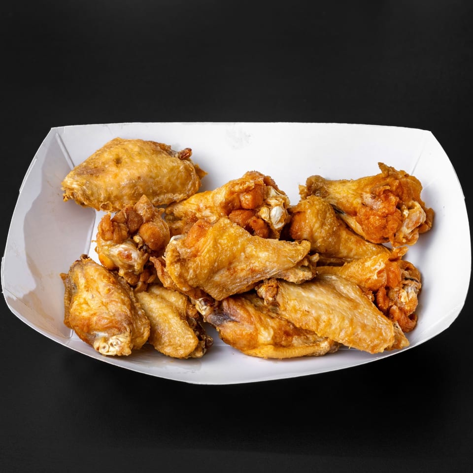 Golden-brown fried chicken wings and drumettes in a white paper tray against a dark background.