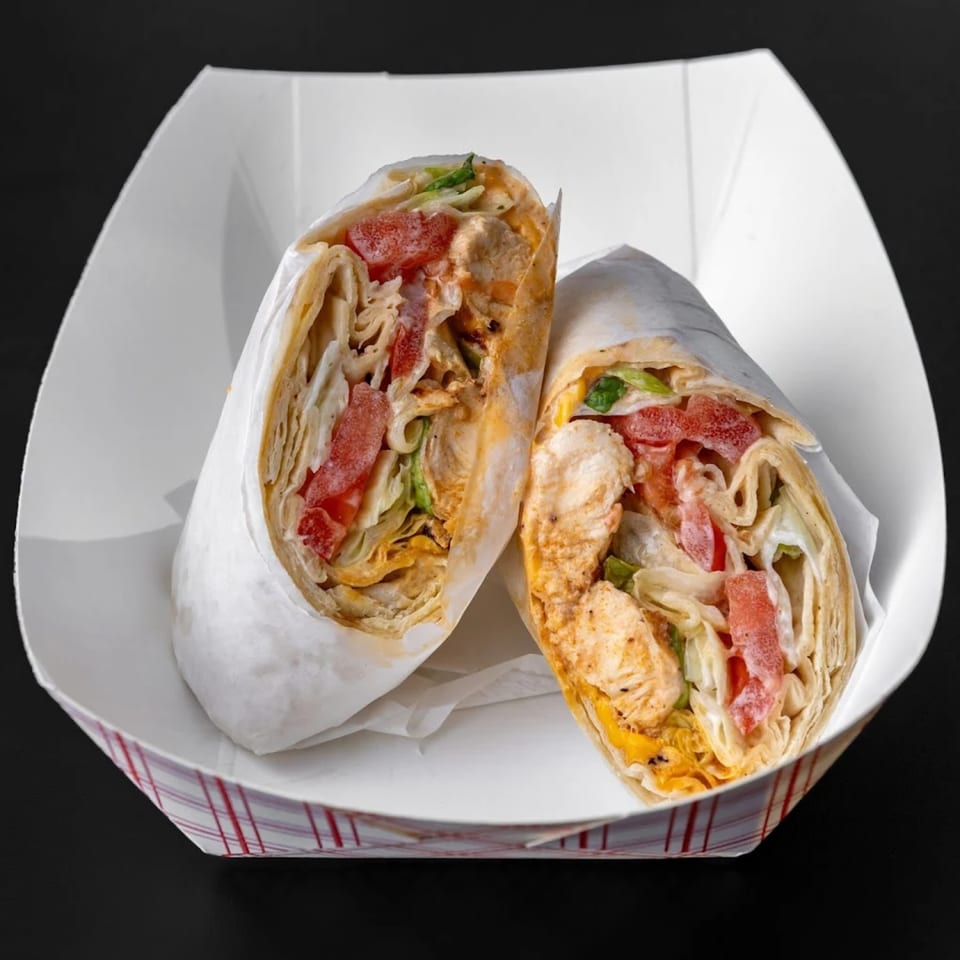 Two chicken wraps with tomatoes, lettuce, and sauce in a white paper tray.